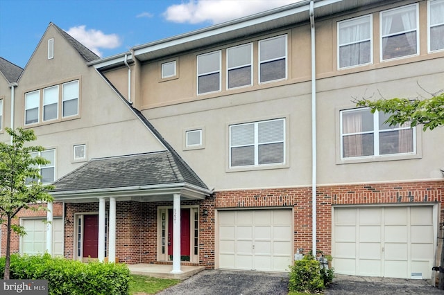 multi unit property featuring a garage, stucco siding, brick siding, and driveway