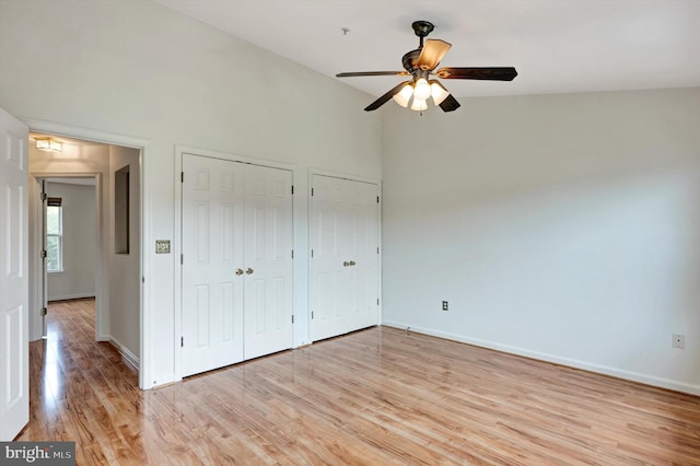 unfurnished bedroom with two closets, baseboards, light wood-type flooring, and a ceiling fan