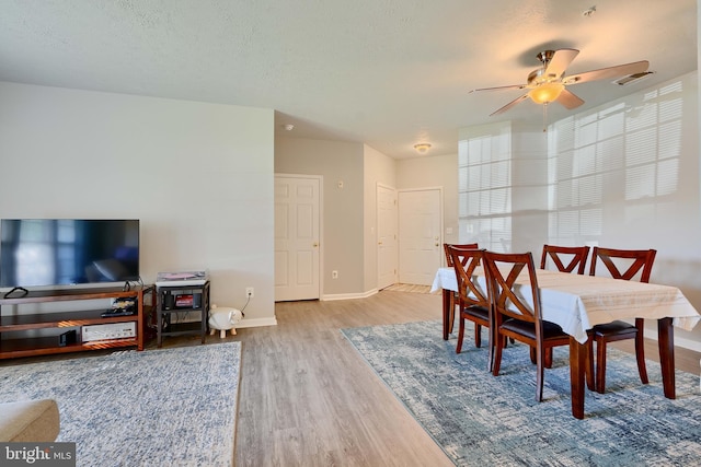 dining room featuring visible vents, wood finished floors, baseboards, ceiling fan, and a textured ceiling