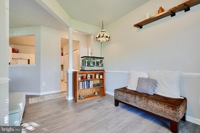 living area with baseboards, decorative columns, and wood finished floors