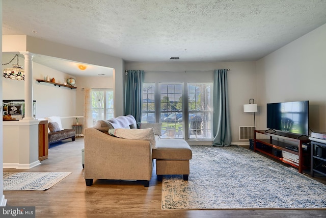 living area featuring decorative columns, a textured ceiling, visible vents, and wood finished floors