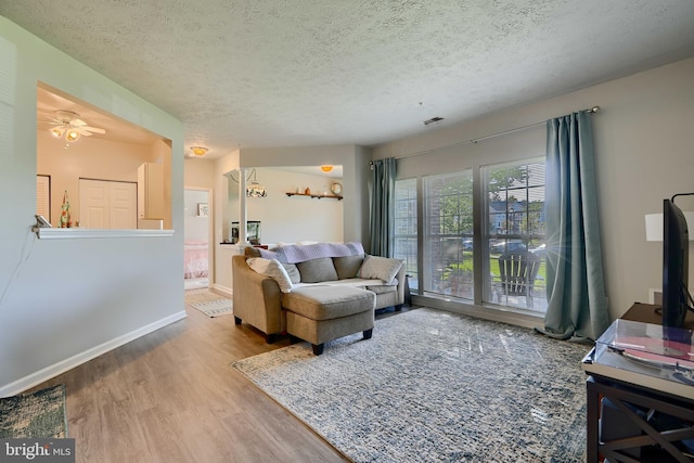 living area with visible vents, wood finished floors, baseboards, ceiling fan, and a textured ceiling