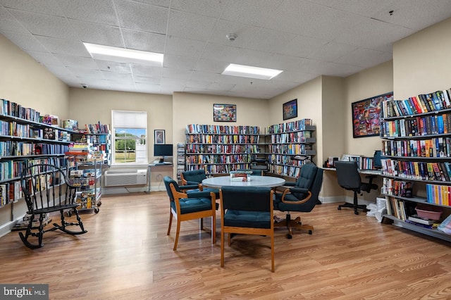 office with a wall mounted air conditioner, baseboards, bookshelves, a drop ceiling, and wood finished floors