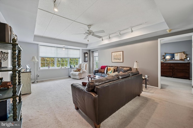 living room featuring track lighting, a raised ceiling, ceiling fan, and light colored carpet
