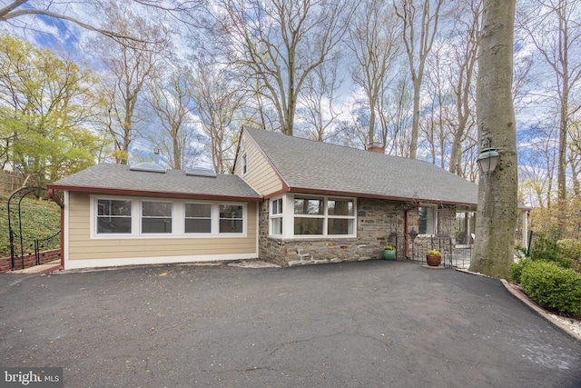 view of front of home featuring roof with shingles, a chimney, aphalt driveway, and stone siding