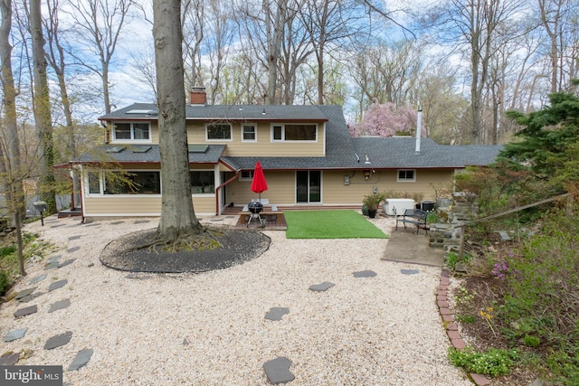 back of property with roof with shingles, a patio, and a chimney