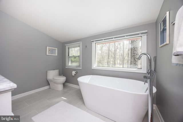 bathroom featuring lofted ceiling, baseboards, toilet, and a soaking tub