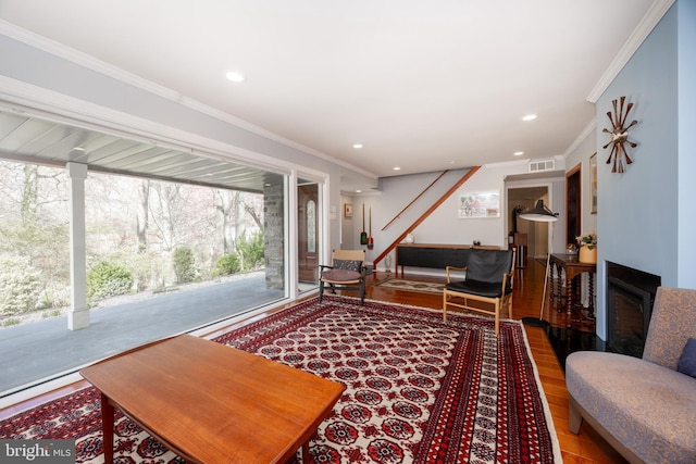 living room with a fireplace, visible vents, ornamental molding, and wood finished floors