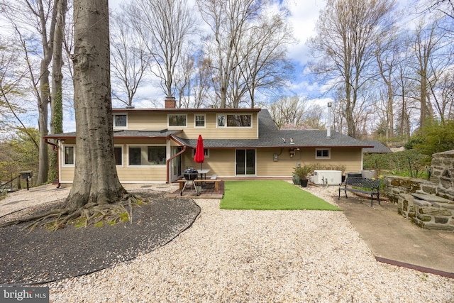 back of house with a patio area, roof with shingles, a lawn, and a chimney