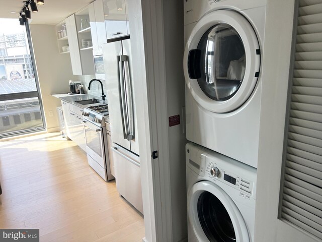 laundry room featuring estacked washer and dryer, light wood-style flooring, and rail lighting
