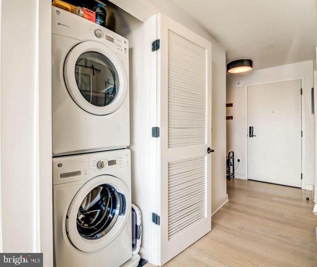 clothes washing area featuring estacked washer and dryer, light wood finished floors, and baseboards