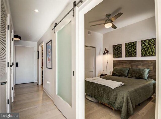 bedroom with a barn door, light wood-style flooring, and a ceiling fan