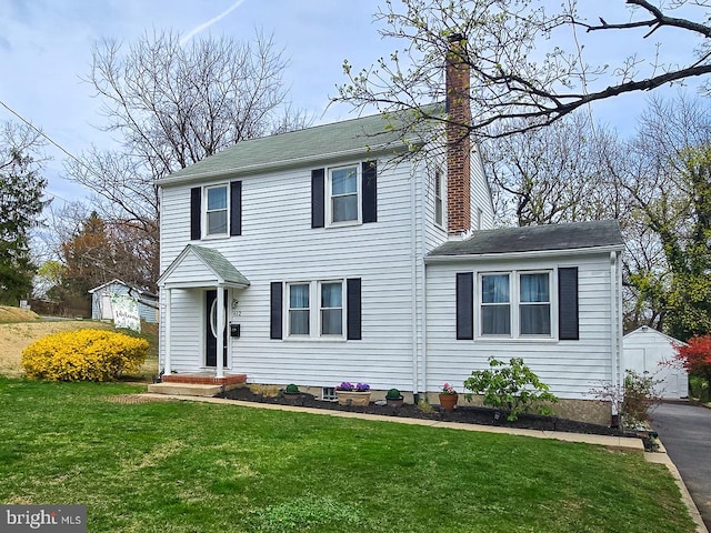 view of front of home with an outbuilding, roof with shingles, a chimney, and a front lawn