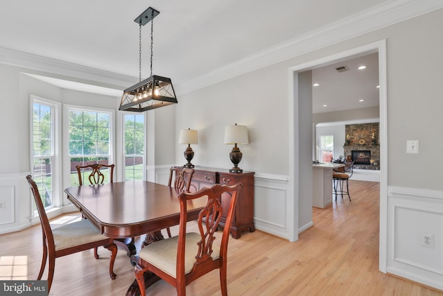 dining space featuring crown molding, light wood-style flooring, wainscoting, and a decorative wall