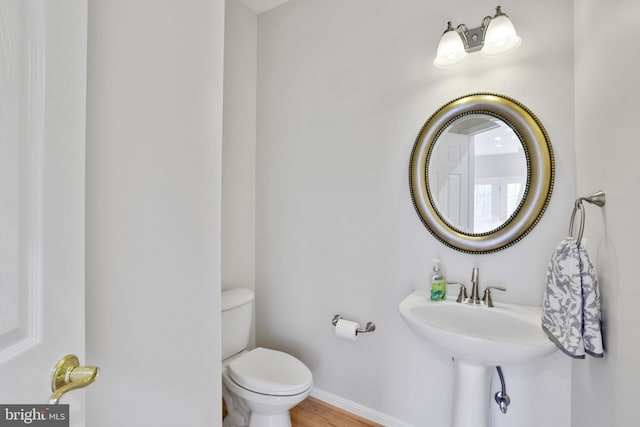 half bathroom with toilet, baseboards, and wood finished floors
