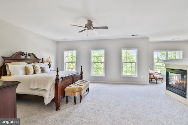 carpeted bedroom with a glass covered fireplace, baseboards, multiple windows, and visible vents