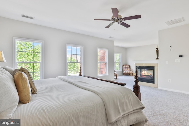 carpeted bedroom featuring baseboards, ceiling fan, a tile fireplace, and visible vents