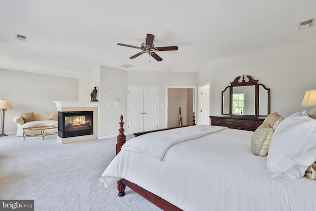 carpeted bedroom with a multi sided fireplace, ceiling fan, and visible vents