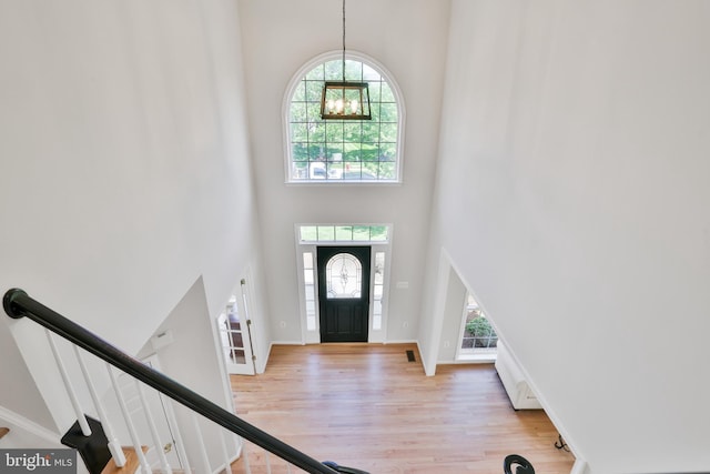foyer featuring baseboards, a high ceiling, an inviting chandelier, and light wood-style flooring