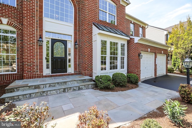doorway to property featuring a standing seam roof, an attached garage, driveway, and brick siding