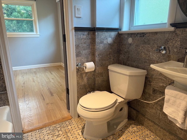 half bath with baseboards, toilet, and tile walls