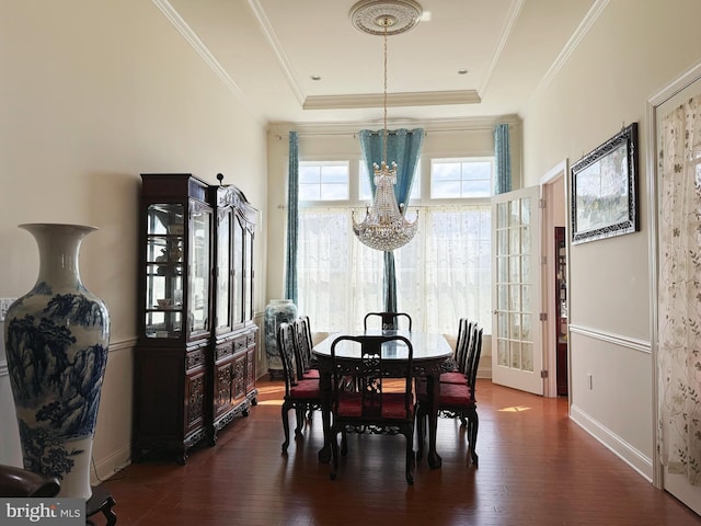 dining space featuring crown molding, a chandelier, a tray ceiling, baseboards, and dark wood-style flooring