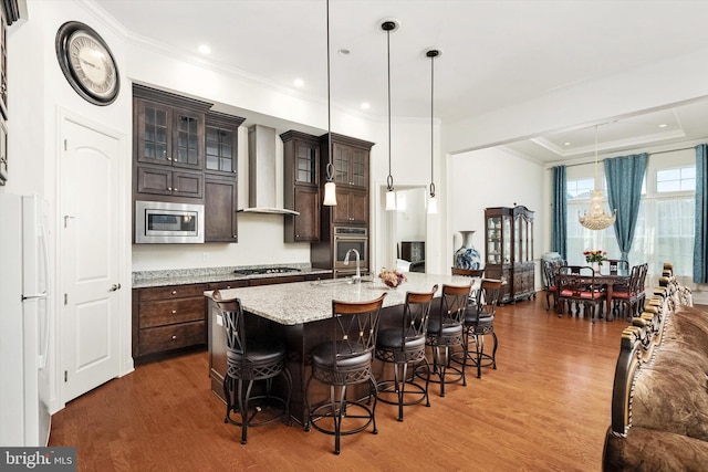 kitchen with a breakfast bar, wood finished floors, a sink, wall chimney exhaust hood, and appliances with stainless steel finishes