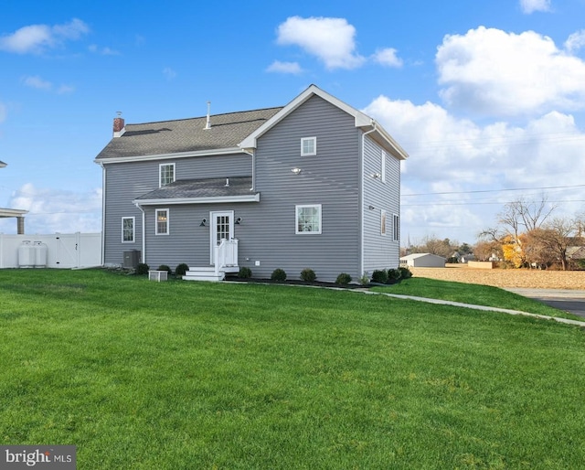 rear view of house with roof with shingles, a chimney, fence, a lawn, and central AC