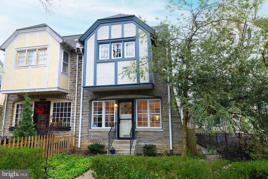 tudor house featuring entry steps, stucco siding, stone siding, and fence