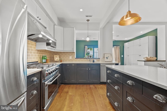 kitchen featuring stainless steel appliances, white cabinetry, under cabinet range hood, hanging light fixtures, and light wood-style flooring