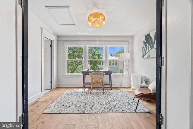 living area with attic access, radiator heating unit, wood finished floors, and baseboards