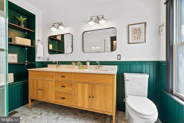 full bath with a wainscoted wall, toilet, and double vanity