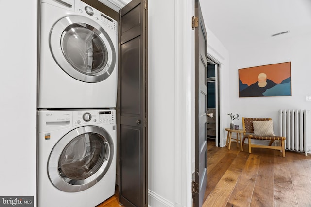 laundry area featuring estacked washer and dryer, radiator, light wood finished floors, and baseboards