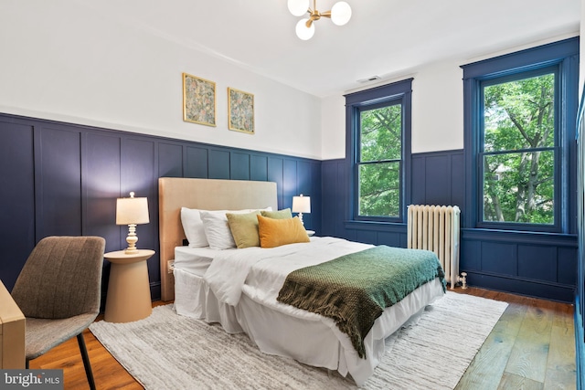 bedroom featuring radiator heating unit, wainscoting, wood finished floors, and a decorative wall