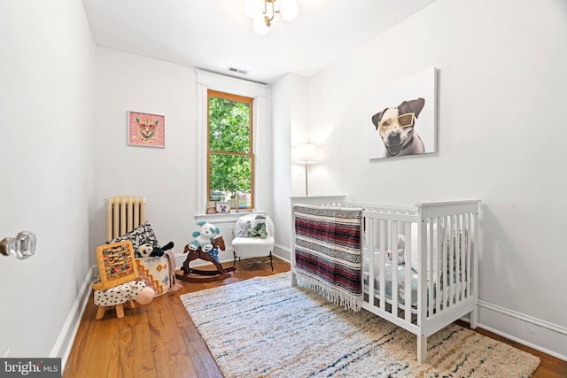 bedroom with radiator heating unit, wood finished floors, a nursery area, and baseboards