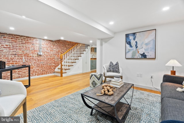 living area featuring brick wall, stairway, baseboards, wood finished floors, and recessed lighting