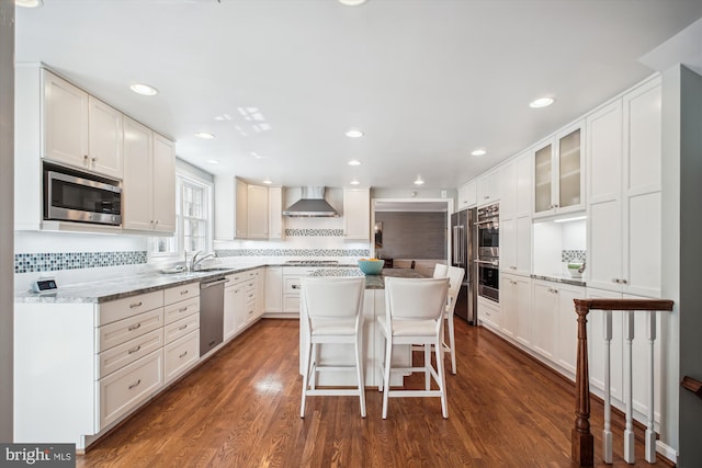 kitchen featuring wall chimney range hood, dark wood-style floors, white cabinetry, stainless steel appliances, and decorative backsplash