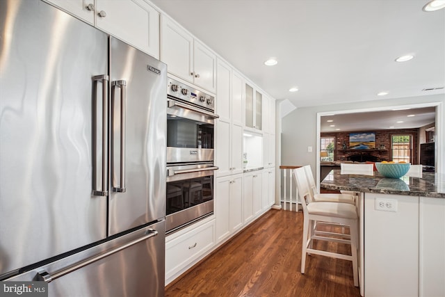 kitchen with dark stone counters, dark wood-type flooring, white cabinets, a breakfast bar, and appliances with stainless steel finishes