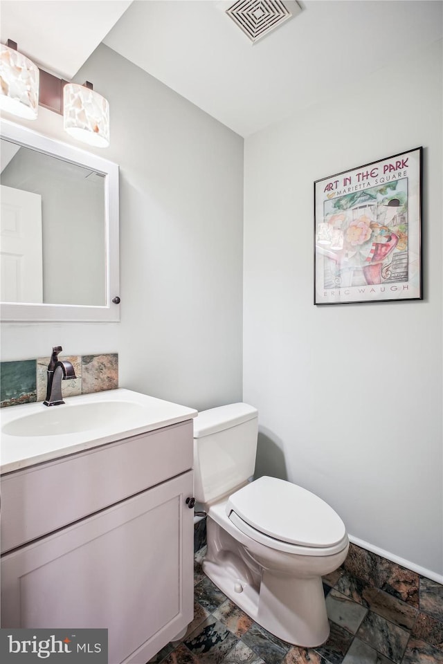 bathroom with stone finish floor, vanity, visible vents, toilet, and baseboards