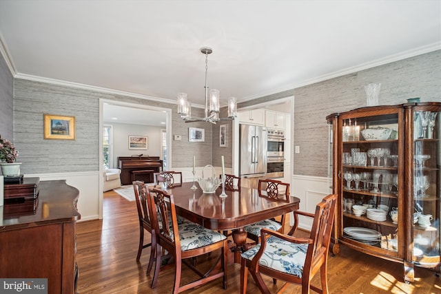 dining space with crown molding, a wainscoted wall, wallpapered walls, a notable chandelier, and dark wood-style floors