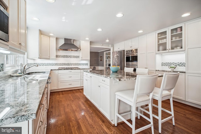 kitchen with wall chimney range hood, a center island, dark wood finished floors, stainless steel appliances, and a sink