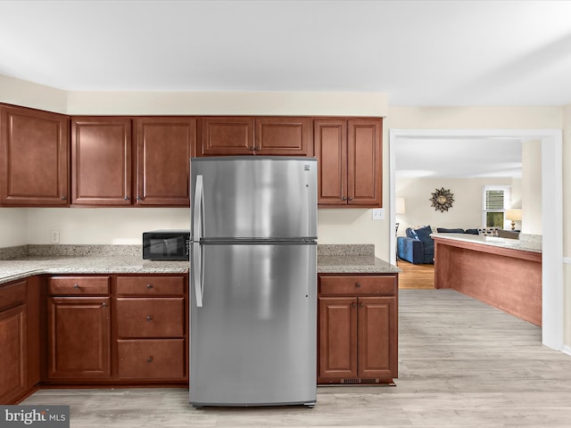 kitchen with black microwave, freestanding refrigerator, light stone counters, and light wood-style floors
