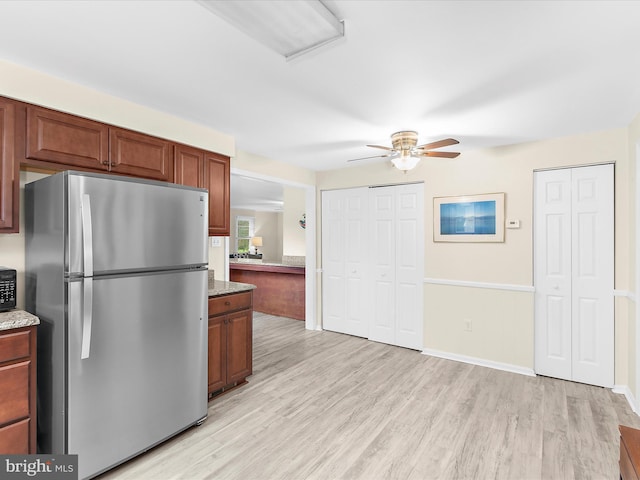 kitchen featuring baseboards, light wood-style flooring, freestanding refrigerator, light stone countertops, and ceiling fan