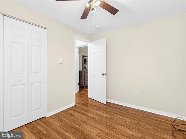 unfurnished bedroom featuring wood finished floors, a closet, a ceiling fan, and baseboards