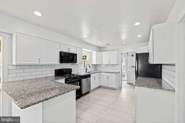 kitchen with a peninsula, washer / clothes dryer, white cabinetry, a sink, and black appliances