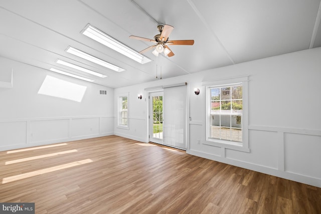 unfurnished room featuring wood finished floors, a decorative wall, plenty of natural light, vaulted ceiling with skylight, and a ceiling fan