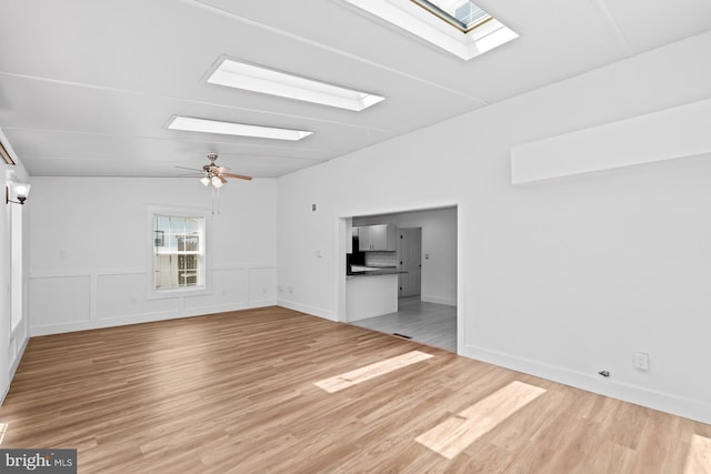 unfurnished living room with a ceiling fan, light wood finished floors, and a skylight