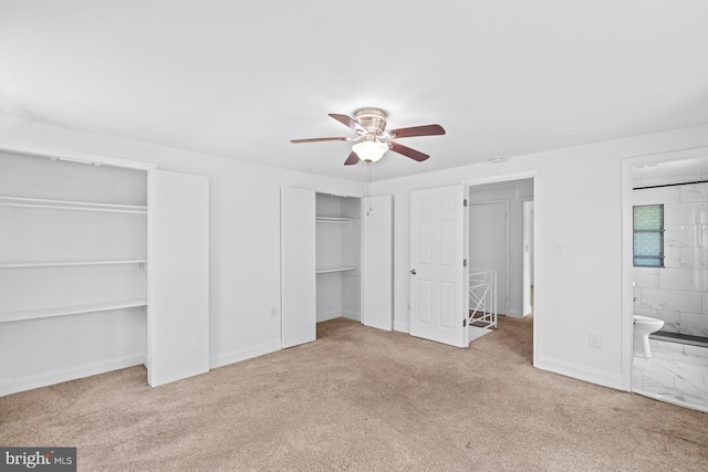 unfurnished bedroom featuring a ceiling fan, two closets, baseboards, carpet flooring, and ensuite bath