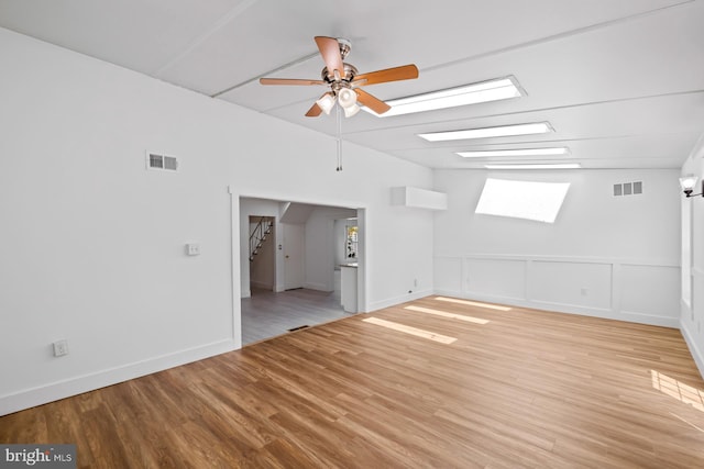 empty room with a ceiling fan, a skylight, visible vents, and wood finished floors