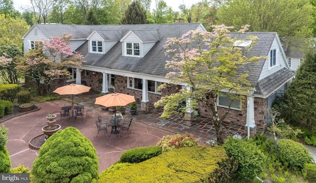 back of house featuring a patio area, stone siding, view of wooded area, and a chimney